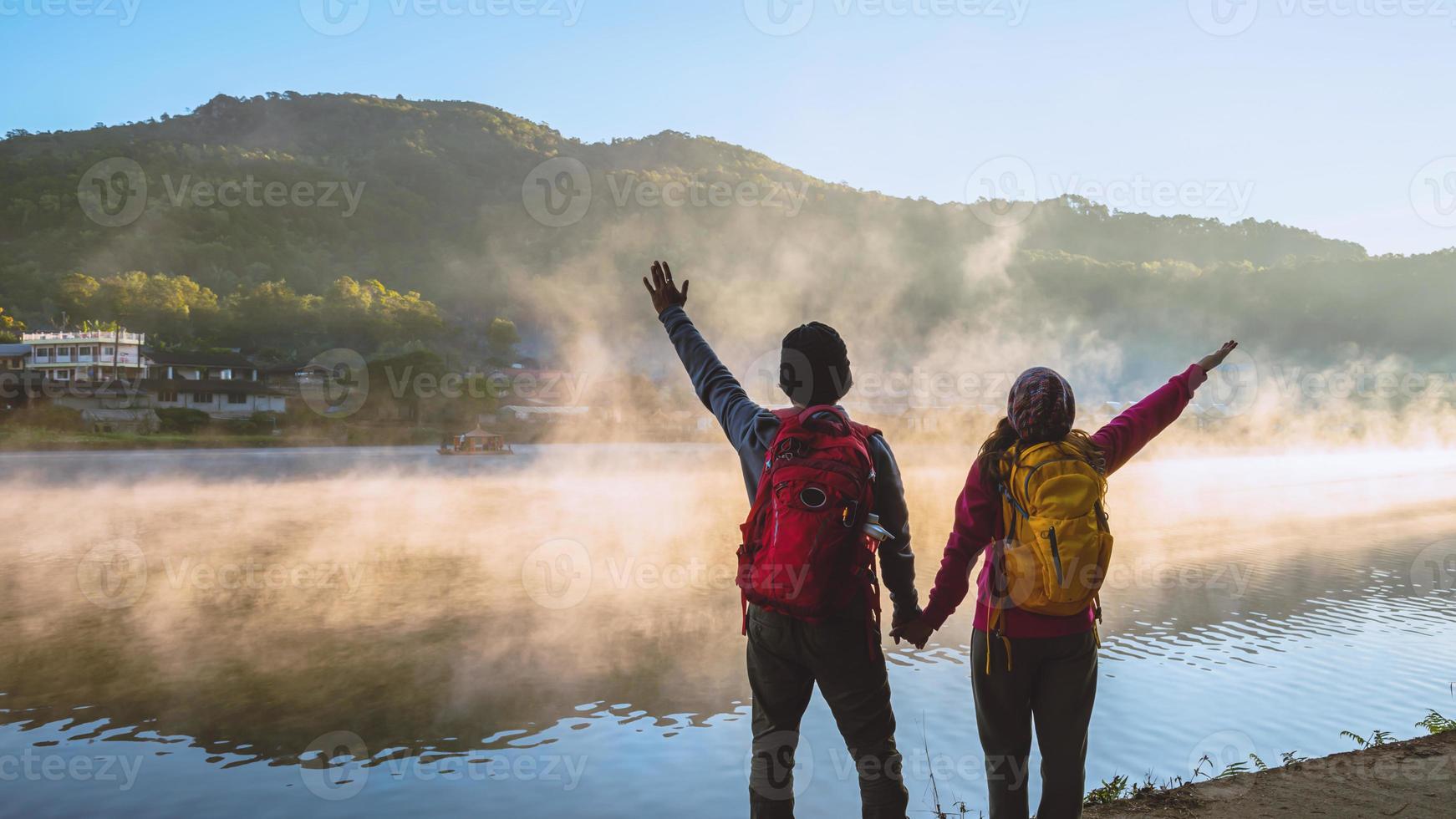 asiatisk kvinna och asiatisk man som backpackade stående nära sjön, hon log, glad och njöt av dimmans naturliga skönhet. foto