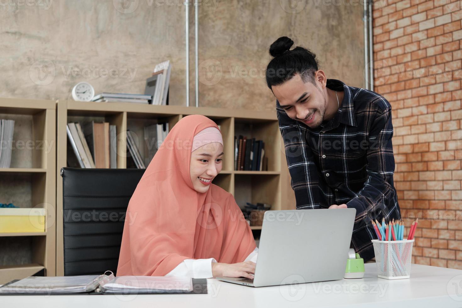 två unga startkollegor som är islamiska människor pratar om framgång med att arbeta i en e-handelsverksamhet med ett leende. använda bärbar dator till online -kommunikation via internet på ett litet kontor. foto