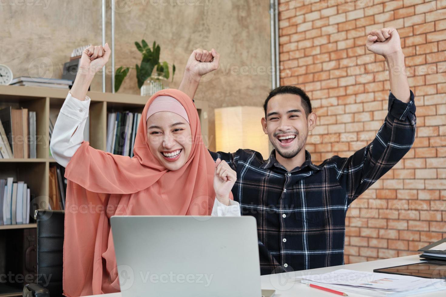 unga startup-partners som är islamiska människor sitter vid ett skrivbord, räcker upp sina händer för att gratulera framgångarna för små kontorsföretag för e-handel. två par kollegor ler och är glada att arbeta. foto