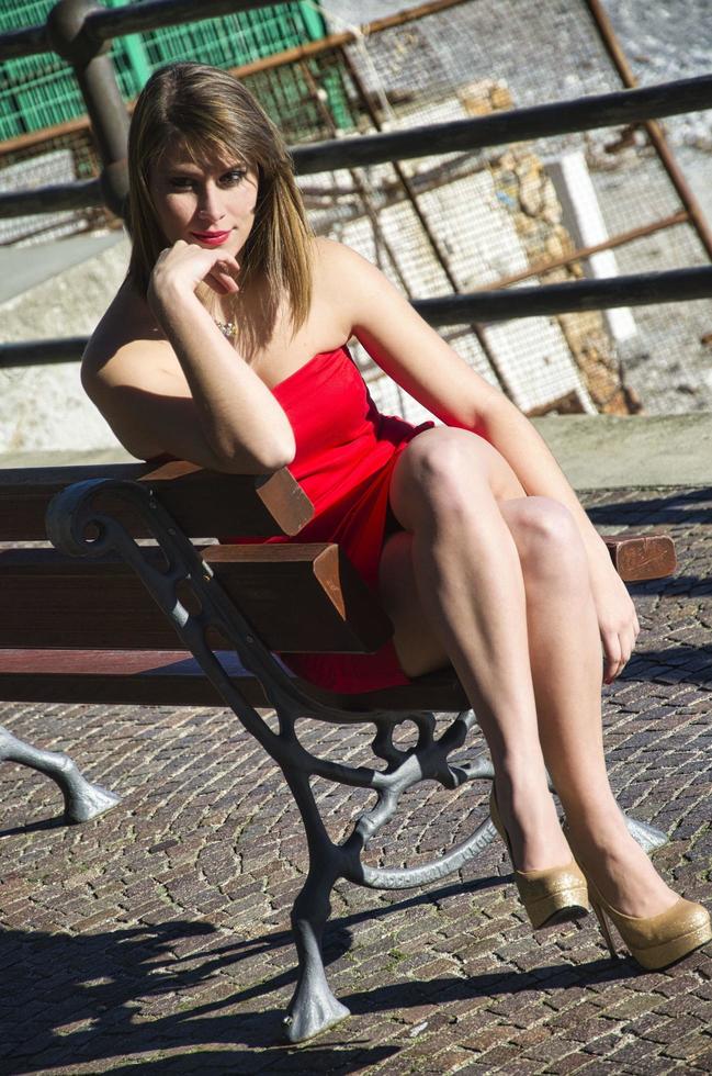 sensuell blond modell sitter på en bänk med benen i kors och handen som håller i hakan foto