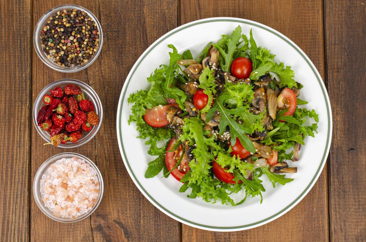 dietsallad av ruccolablad, tomater och stekt svamp på träbord. studiofoto foto