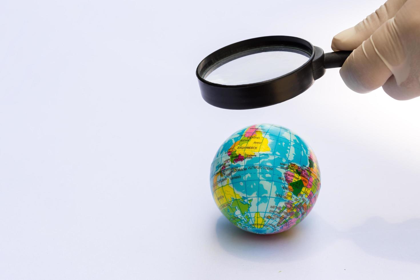 person hand som bär gummihandskar håller förstoringsglas för att se shine globe. isolerade vit bakgrund. koncept som bryr sig om vår värld. foto