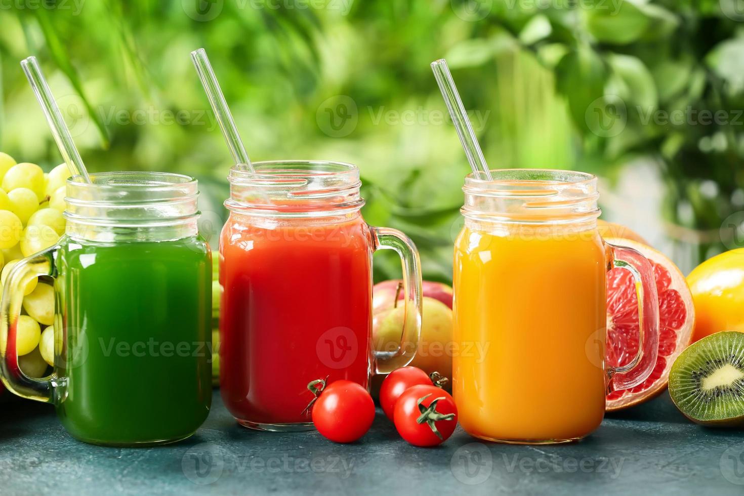mason burkar med hälsosam juice, frukt och grönsaker på bordet utomhus foto