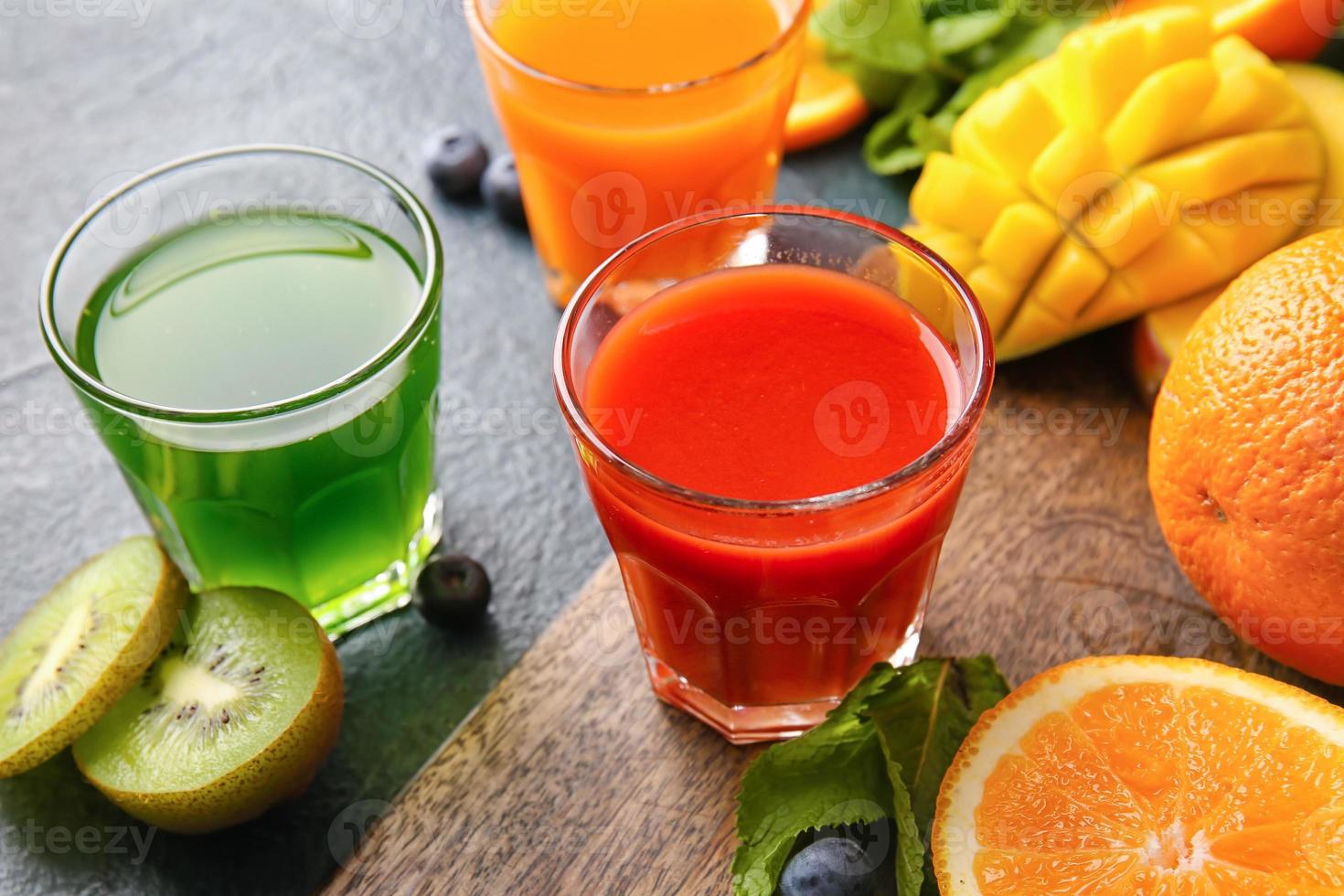 glasögon med hälsosam juice, frukt och grönsaker på mörk bakgrund foto