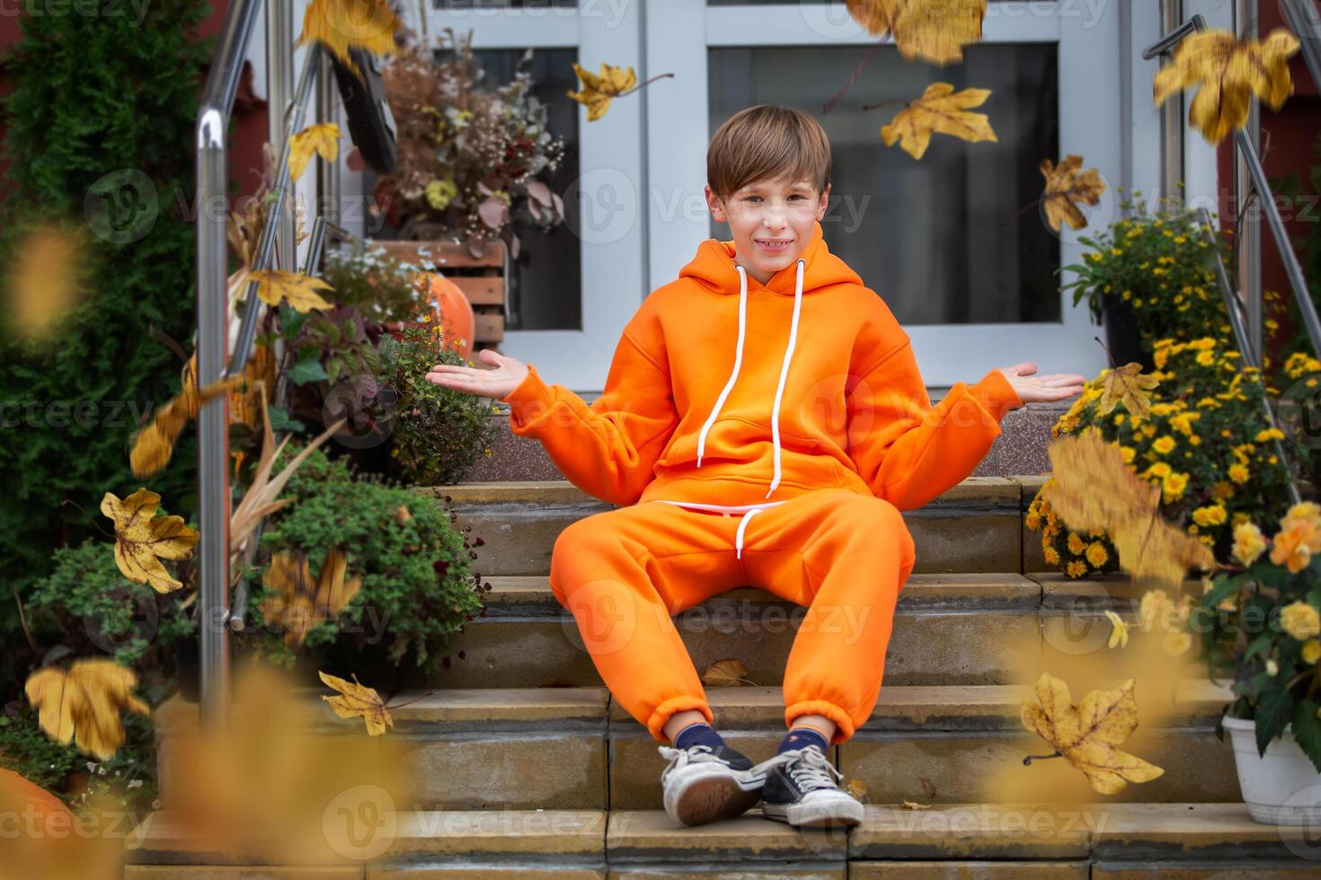 en pojke i orange kläder sitter på de steg och utseende på de gul flygande höst löv. foto