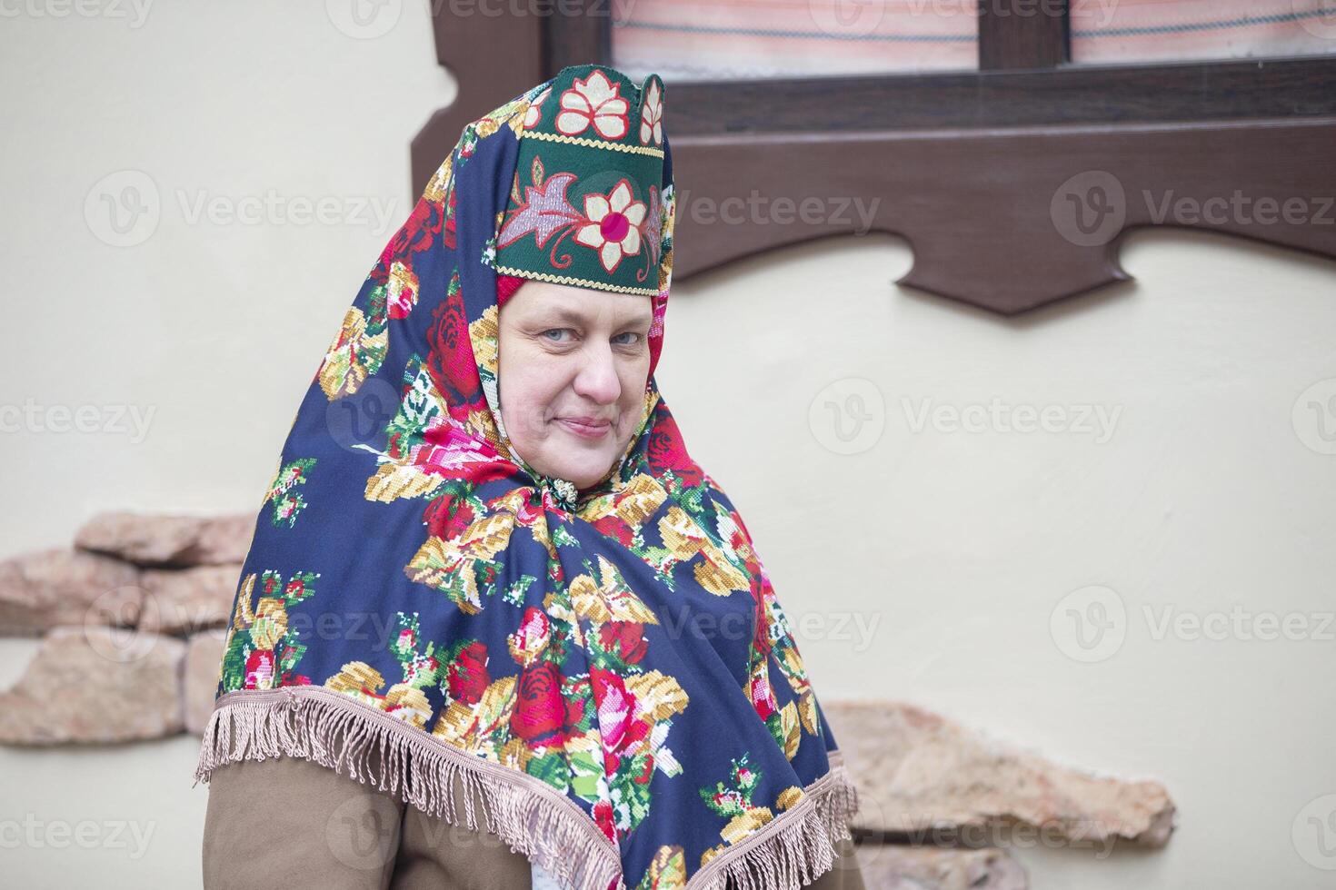 ett äldre ryska kvinna i en traditionell huvudbonad, kokoshnik, poser mot de bakgrund av en by hus. foto