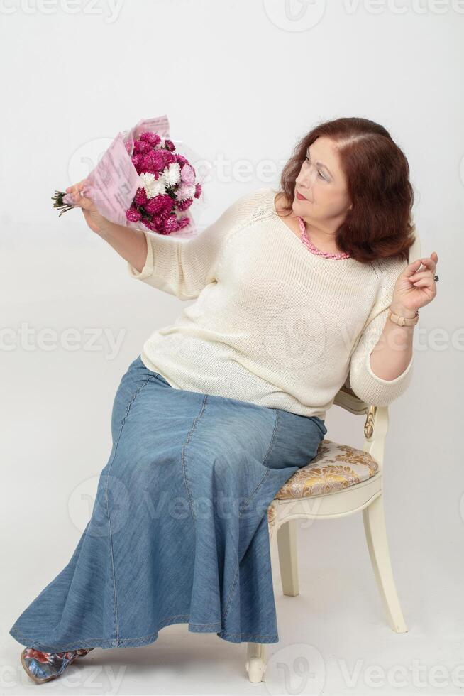 en skön äldre kvinna är ser på en gåva bukett av blommor. foto