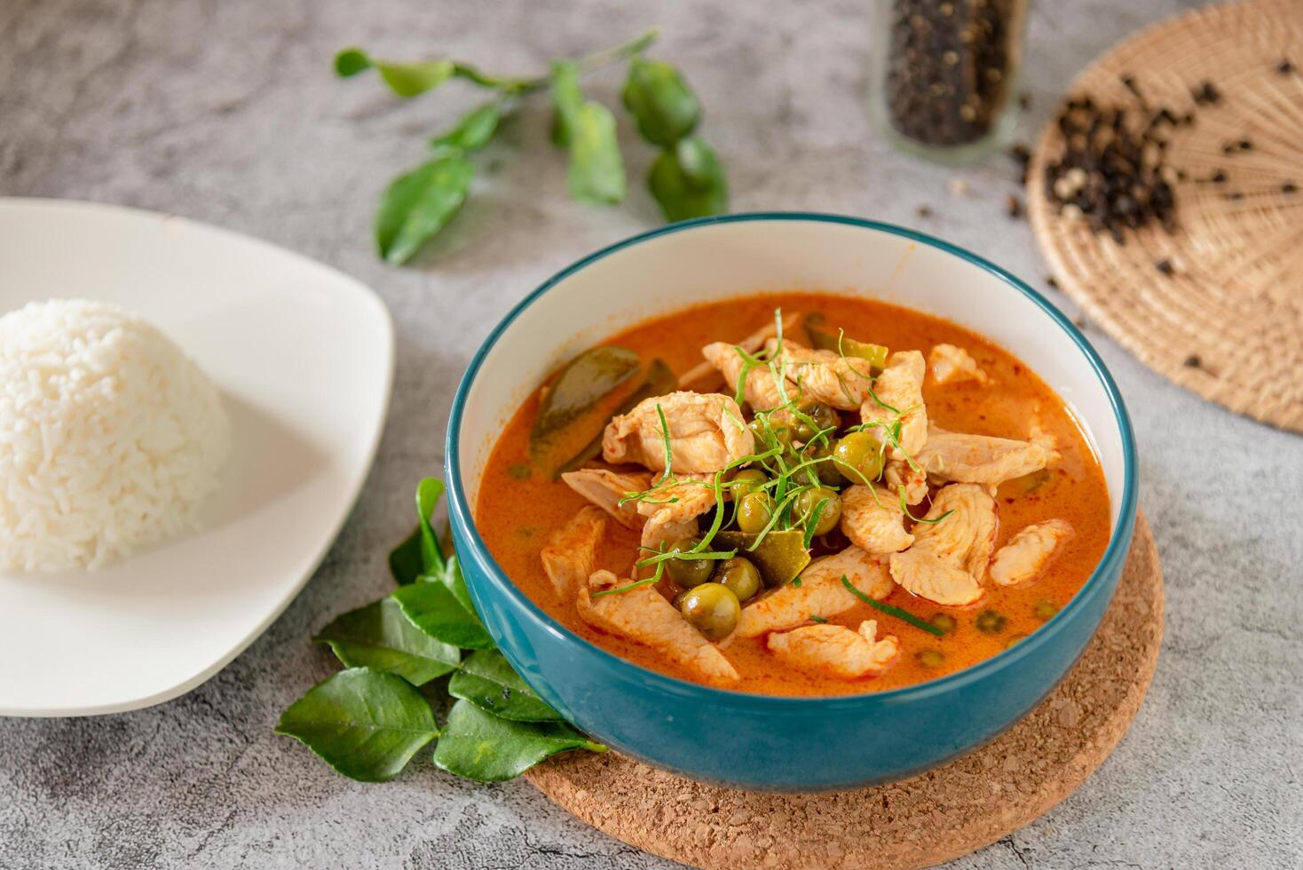 stängd upp thai röd curry med kyckling, färsk vegetabiliska och ört i skål, tjäna med ångad ris foto