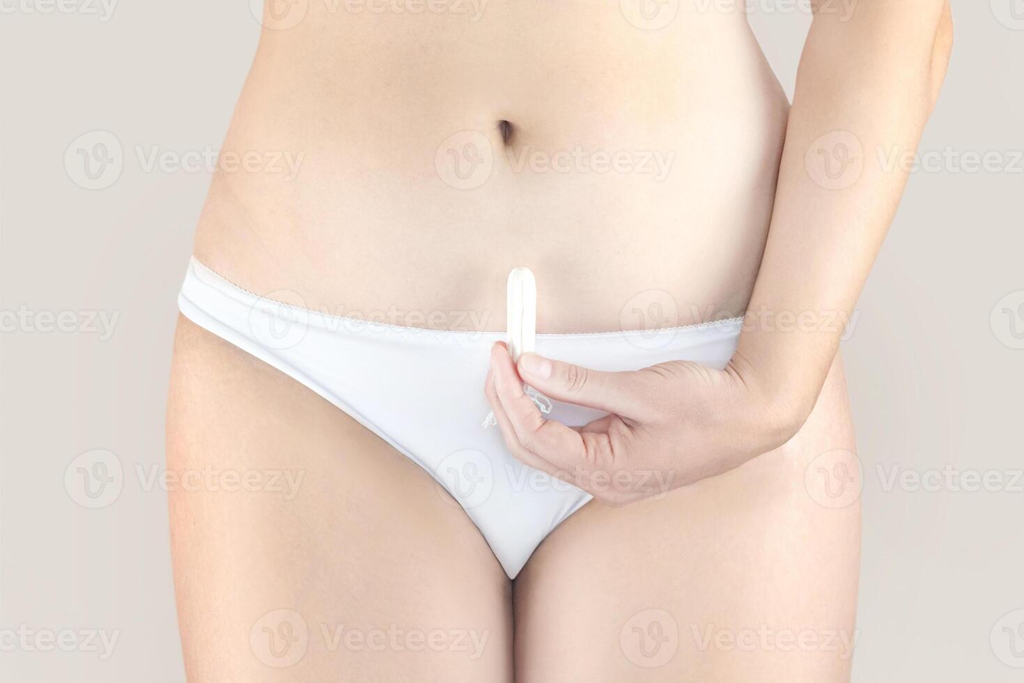 kvinna innehav en menstruation bomull tampong i henne hand, i vit underkläder naken beige bakgrund stänga upp foto