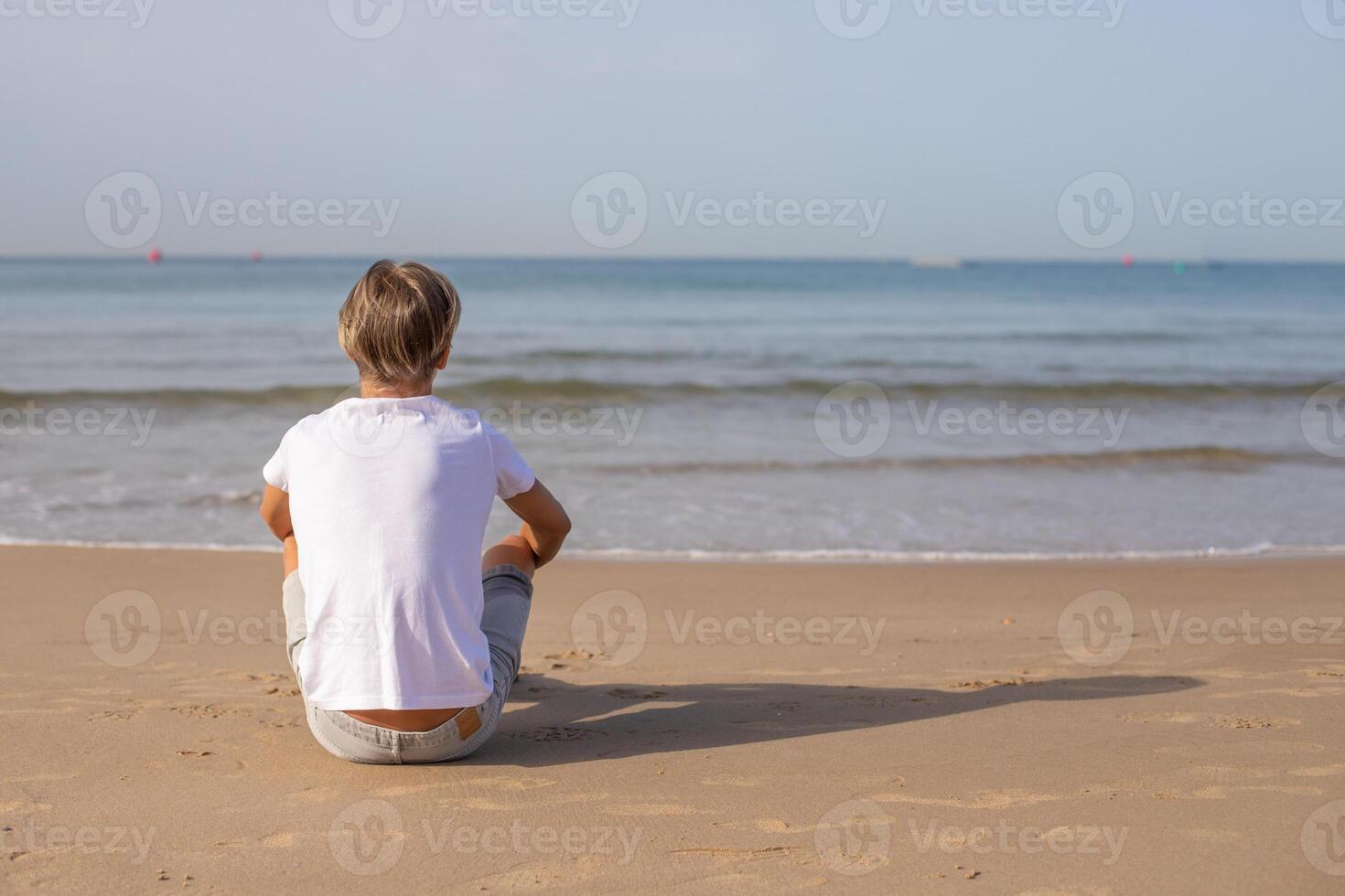 stänga upp tillbaka se stilig tonåring pojke i vit t-shirt Sammanträde på de strand och njut av en sommar semester ser bort, med Plats för text.familj semester, semester, resa, resor begrepp. foto