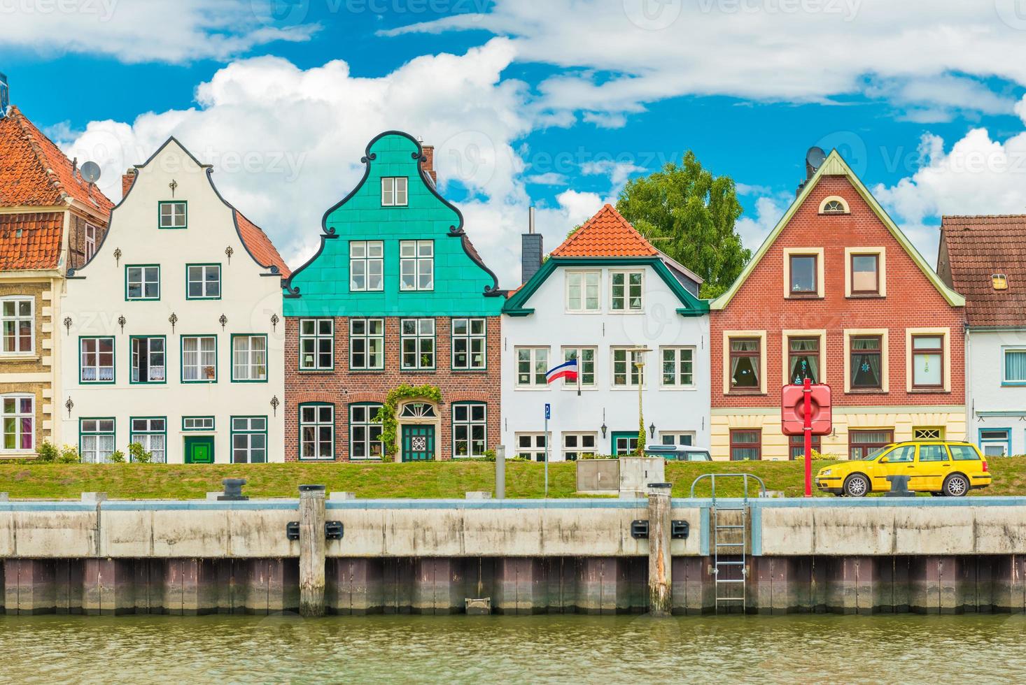 liten vacker europeisk stad. fasader av de gamla historiska färgade husen. gul bil parkerad på flodvallen. gluckstadt, Tyskland foto