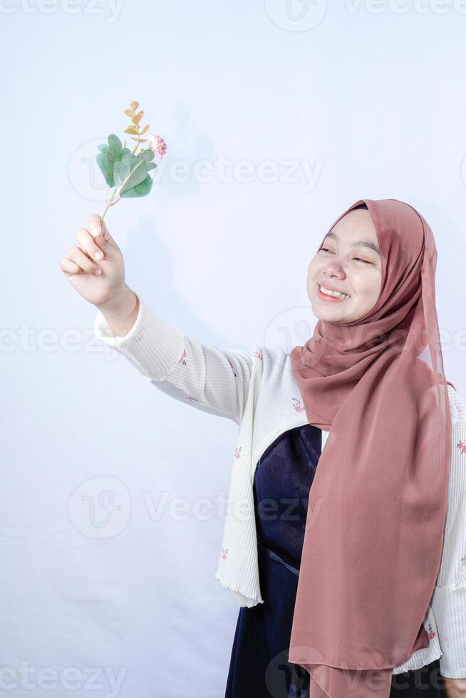 en förtäckt javanese kvinna är ser på en blomma hölls upp i henne hand mot de bakgrund av ett tömma Plats för fotokopiering. foto