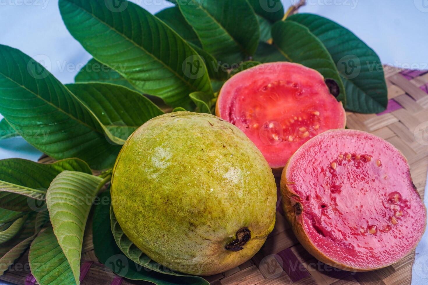 guava isolerat. samling av röd kött guava frukt med gulaktig grön hud och löv isolerat på en vit bakgrund med bambu matta. foto