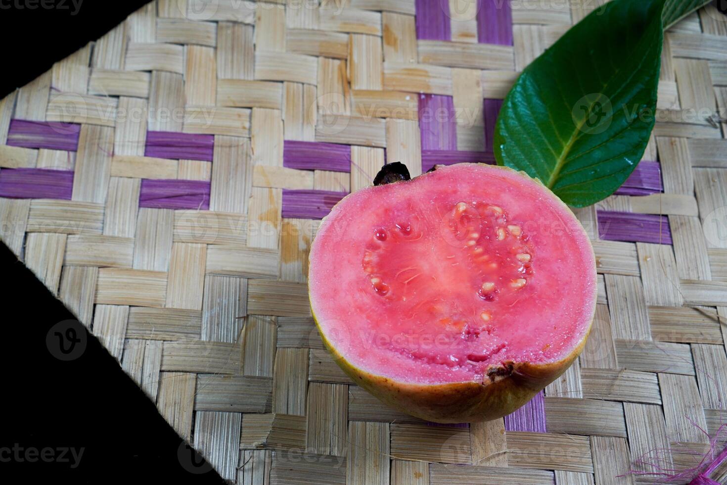 guava isolerat. guava frukt med röd kött med gulaktig grön hud och löv isolerat på en svart bakgrund med vävd bambu som en bas. foto