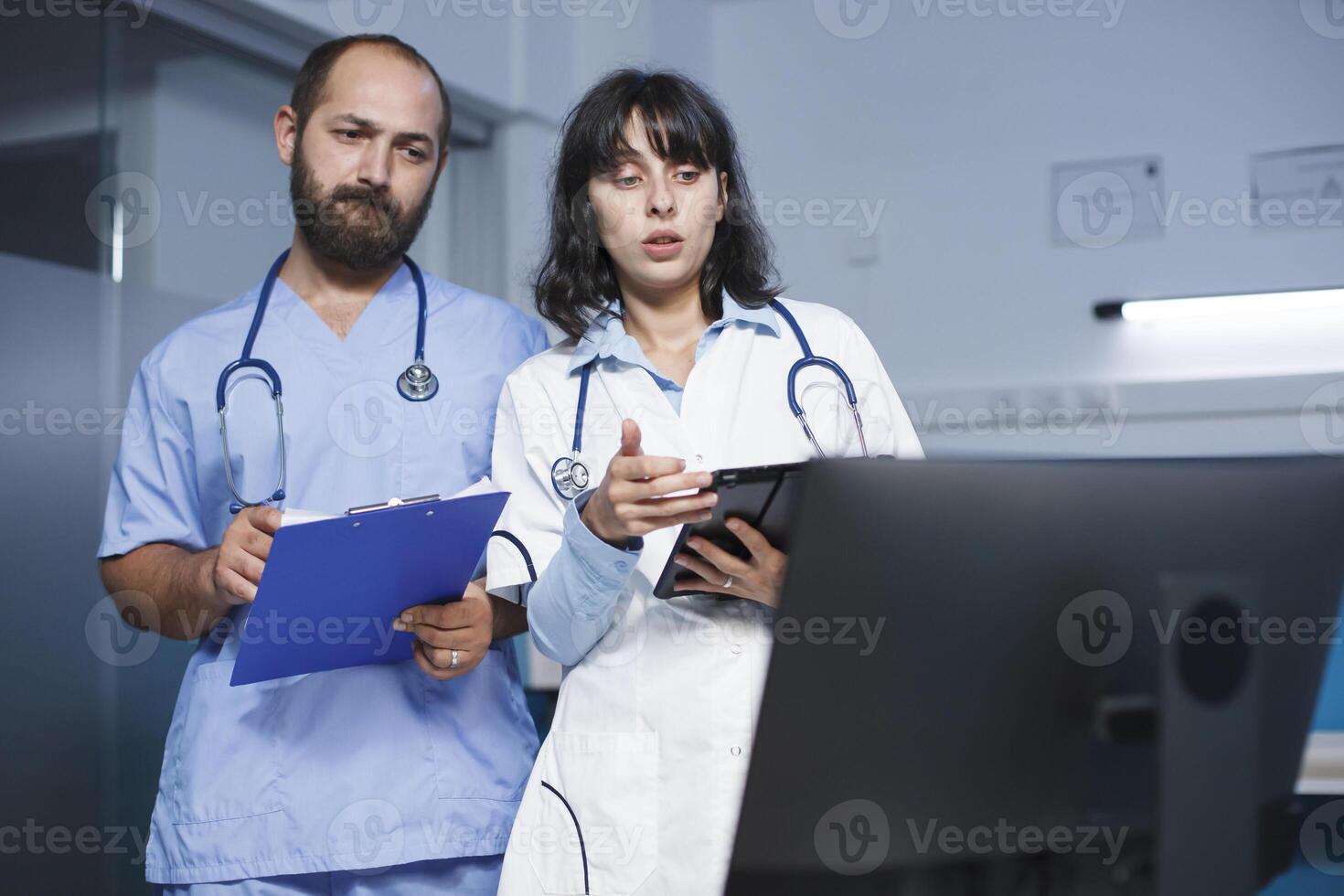 caucasian man med en Urklipp talande handla om patient möten med en kvinna innehav en digital läsplatta i de klinik. kvinna läkare diskuterar sjukvård och medicin med en manlig sjuksköterska. foto