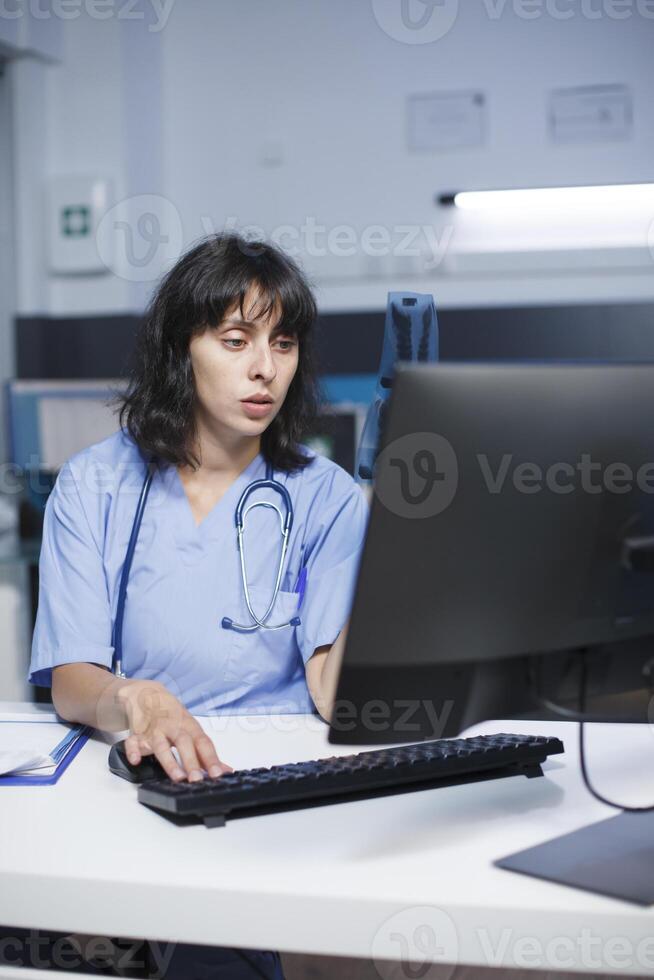 på de klinik kontor skrivbord, en fast besluten caucasian sjuksköterska checkar och analyser henne anteckningar. närbild skott av läkare i blå scrubs få redo till ser människor för medicinsk samråd. foto
