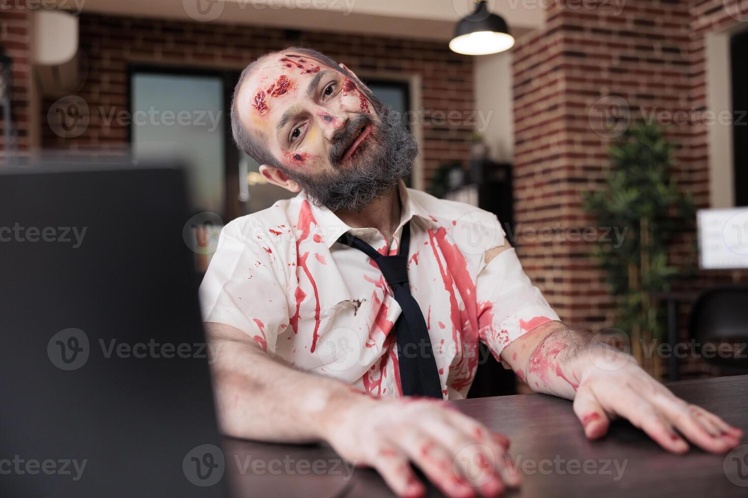 porträtt av överarbetad man med dåsig uttryck, haltande på kontor skrivbord stol, ser tycka om zombie. affärsman täckt i blod, ser utmattad efter arbetssätt för mycket, utnyttjas förbi kapitalism foto
