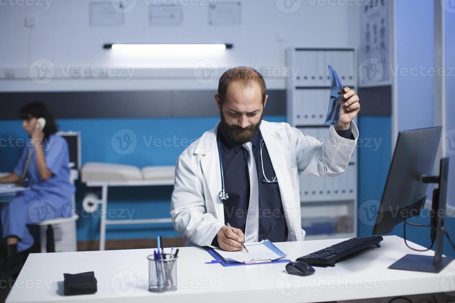 tillägnad medicinsk läkare undersöker en ct bild av en patient medan tar anteckningar på hans urklipp. de bild skildrar en caucasian manlig sjukvård arbetstagare granskning en bröst röntgen avbildning av en person. foto