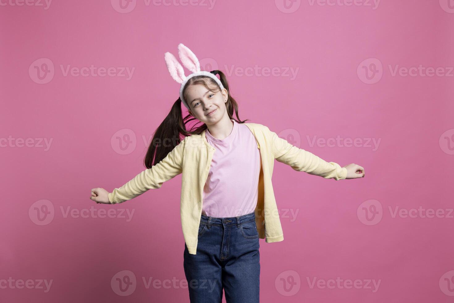 Lycklig skol med pigtails och kanin öron dans i studio, som visar modern härlig dansa rör sig i främre av kamera. ung barn fira påsk Semester fest, sorglös junior. foto