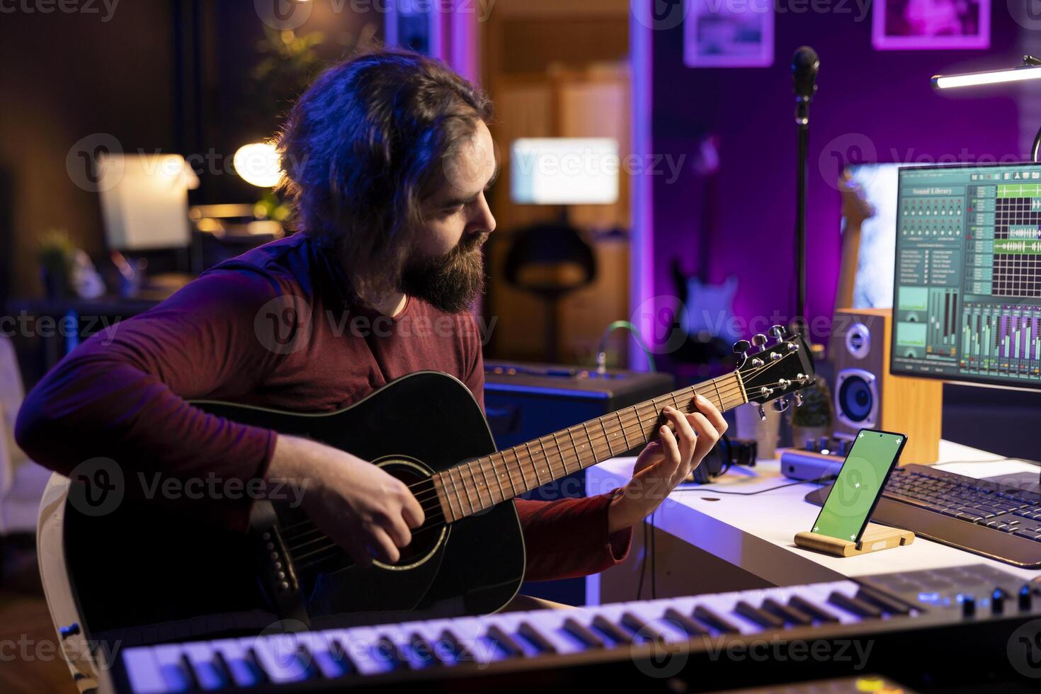 musiker spelar akustisk instrument Nästa till grönskärm på smartphone, inlärning ny överenskommelser på strängar till spela på gitarr. konstnär producent utvecklande hans musikalisk Kompetens i hans Hem studio. foto