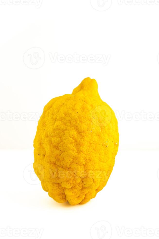 en stor, grov texturerad citron- sitter mot en enkel vit bakgrund. dess ojämn yta och vibrerande gul Färg skapa en slående kontrast, betona dess färsk och organisk utseende. foto
