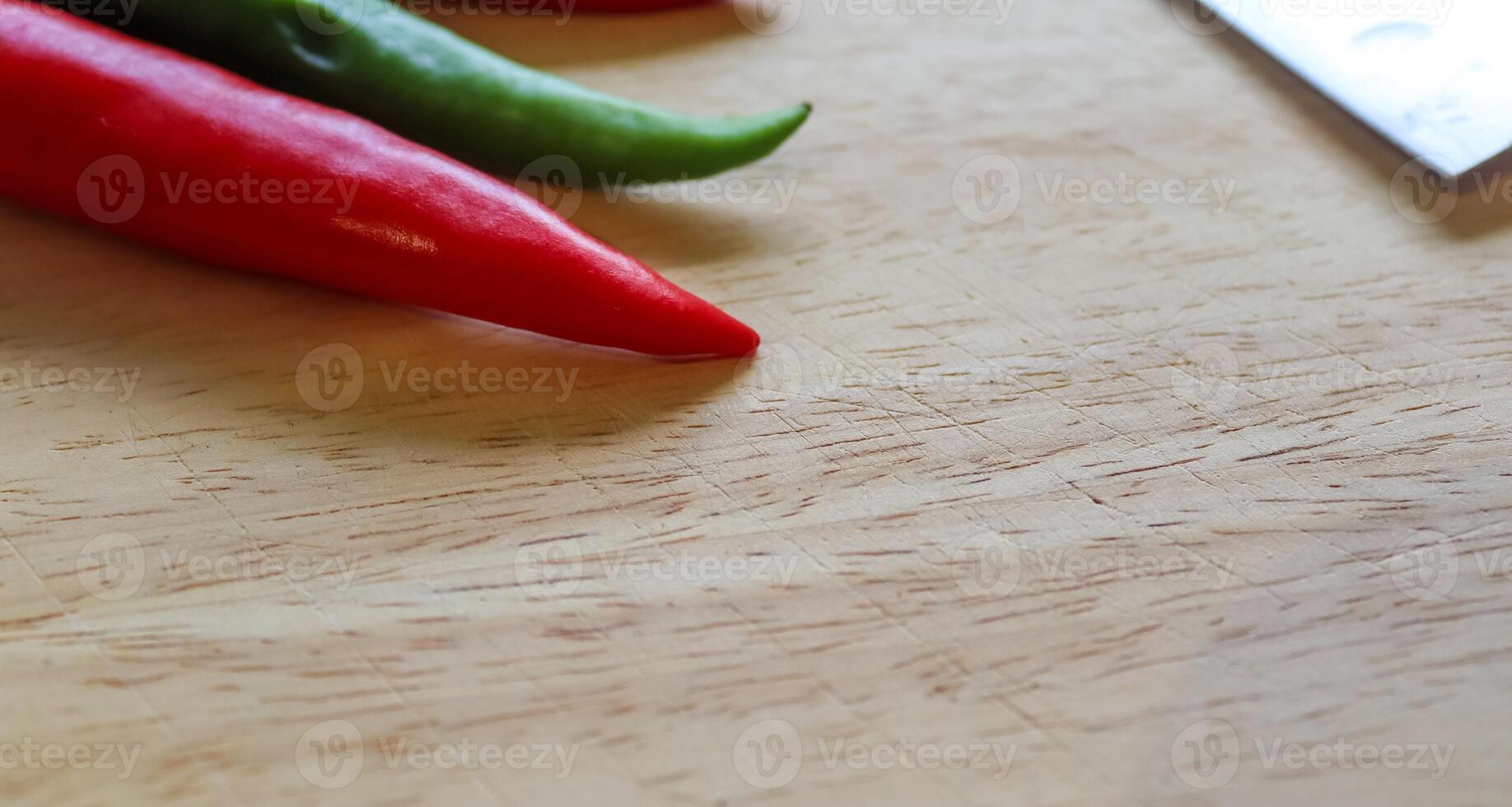 topp- och perspektivvy av chilipeppar och stålkniv på en träskärbräda med en isolerad bakgrund foto