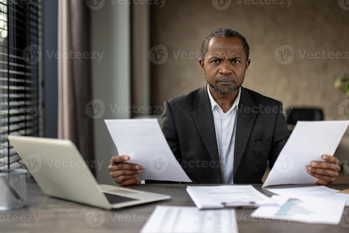 mogna afrikansk amerikan affärsman i en kostym rynkar pannan som han recensioner Viktig dokument, reflekterande en stressig ögonblick i en professionell miljö. foto