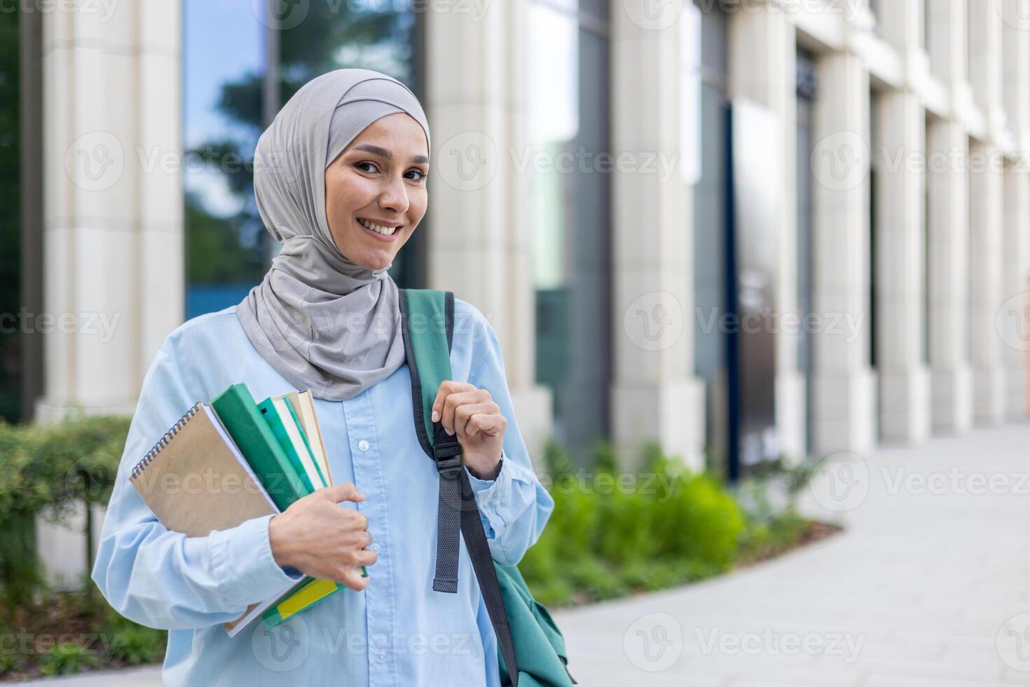 ett elegant ung muslim kvinna i hijab bärande böcker, lyckligt gående i en företag distrikt, reflekterande urban professionell liv. foto