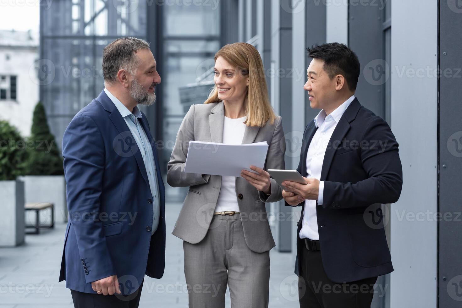 internationell företag team möte mogna man, caucasian kvinna, asiatisk anställd kommunicera . grupp av entreprenörer i formell kostymer diskutera en projekt dokumentera nära kontor Centrum på gata foto