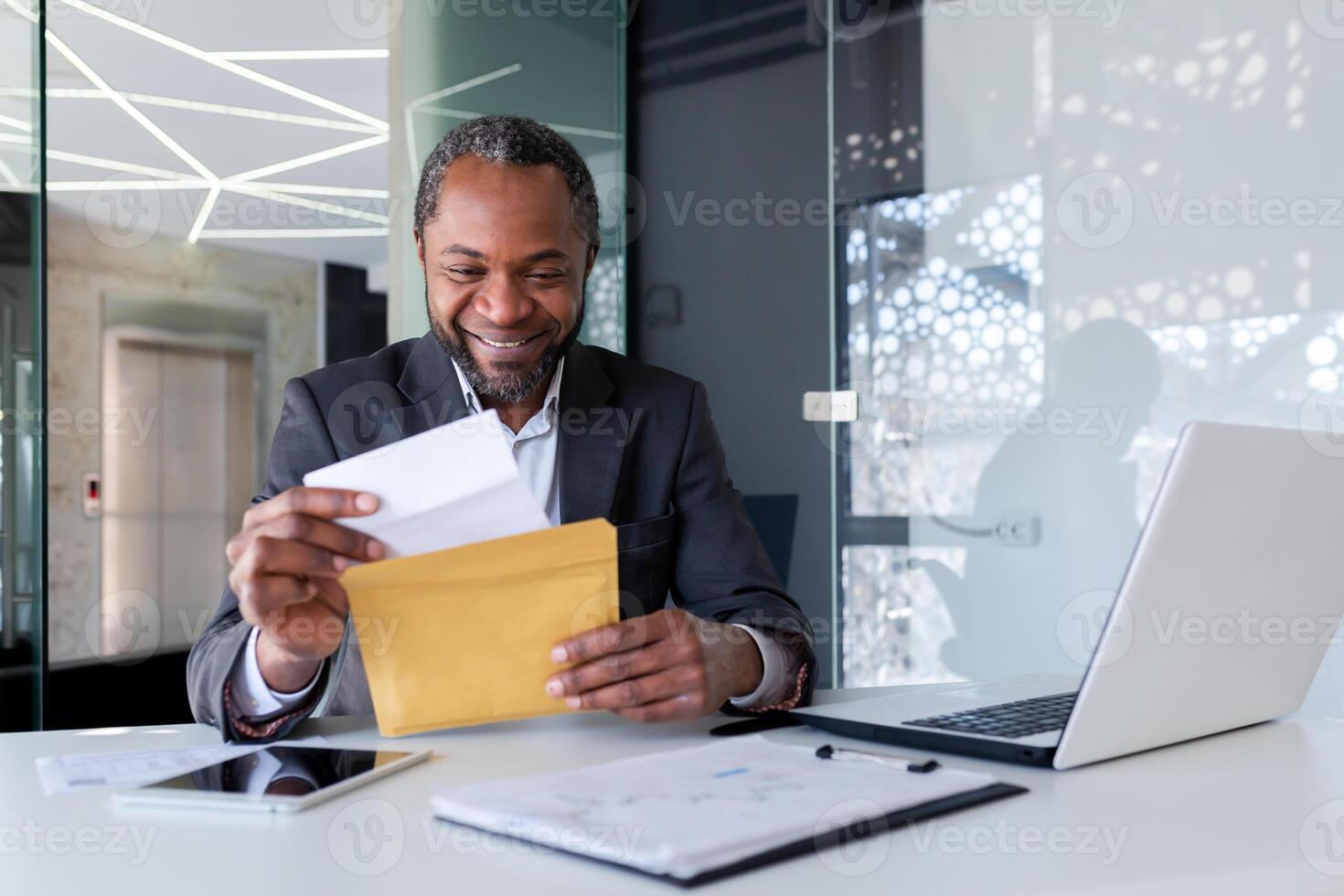afrikansk amerikan affärsman läsning Bra Nyheter, man inuti kontor arbetsplats innehav post kuvert brev med Bra Nyheter, chef i företag kostym mogna och vuxen. foto