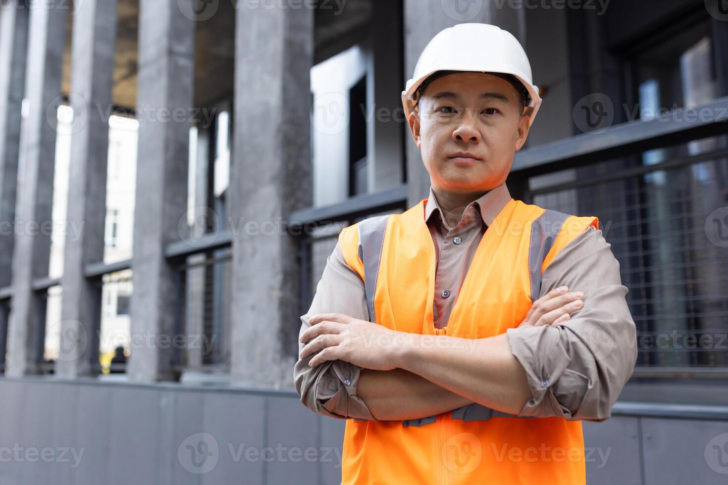 porträtt av en allvarlig ung asiatisk manlig ingenjör arkitekt bär konstruktion Hardhat och hus, höjning hans händer och ser självsäkert på de kamera. foto