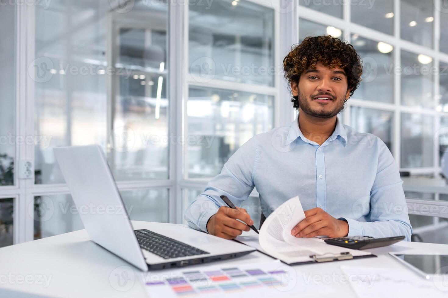 porträtt av ung chef inuti kontor på arbetsplats, framgångsrik latinamerikan affärsman leende och ser på kamera, man signering kontrakt och fakturor, finansiär leende och ser på kamera. foto