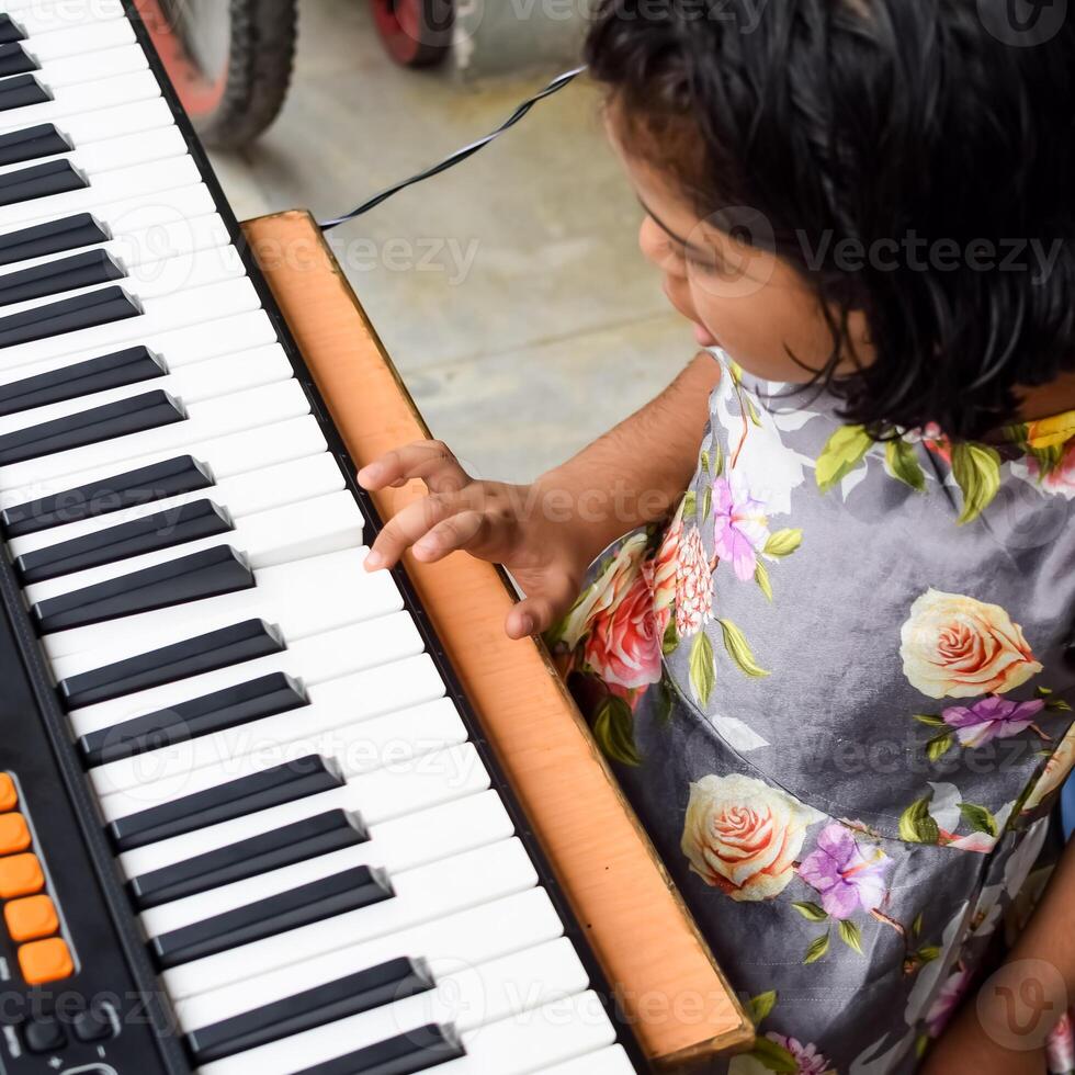 asiatisk söt flicka spelar de synthesizer eller piano. söt liten unge inlärning på vilket sätt till spela piano. barnets händer på de tangentbord inomhus. foto