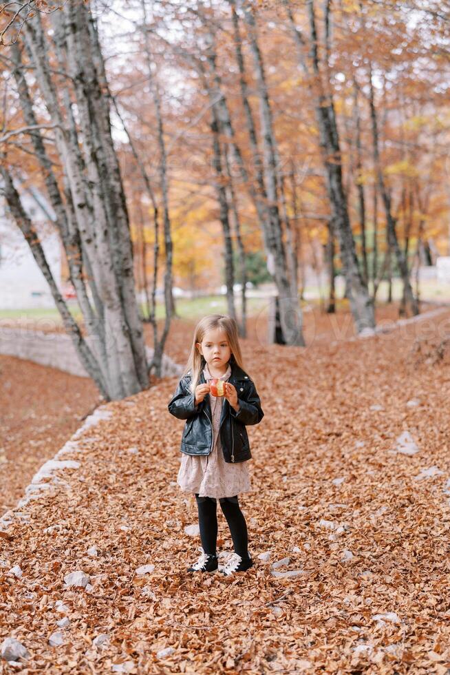 liten flicka med ett äpple i henne hand står tänkande i de höst skog foto