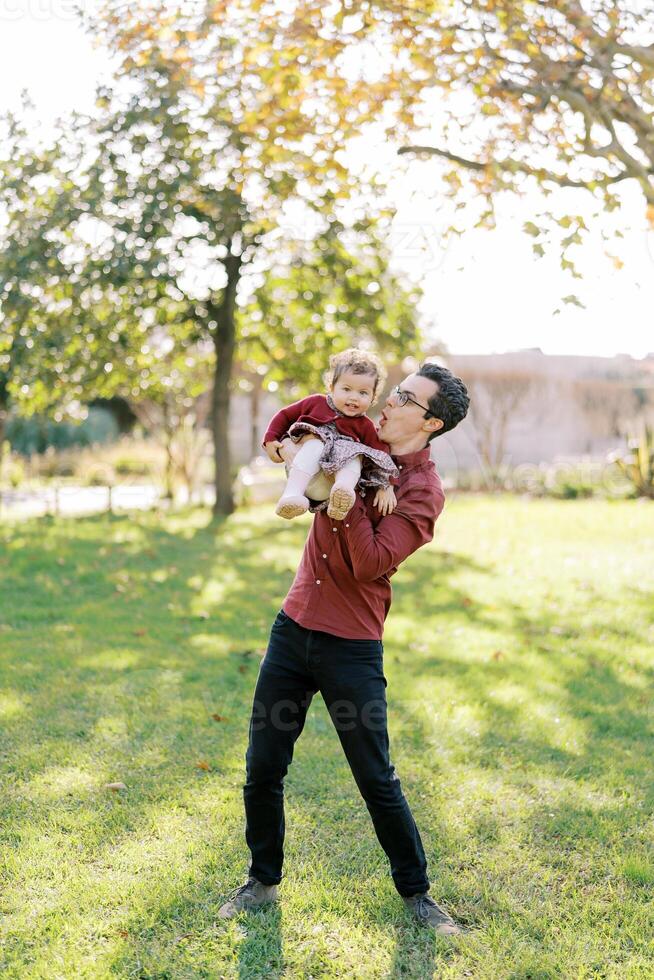 leende pappa innehav en liten flicka i hans vapen lutande till de sida foto