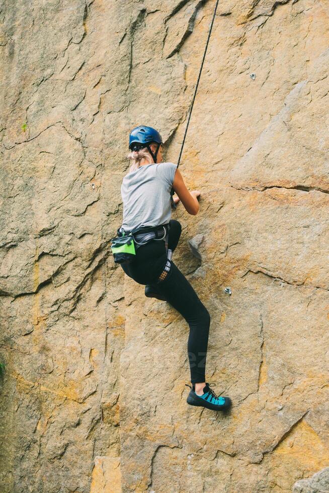 ung atletisk kvinna i Utrustning håller på med sten klättrande utomhus. Träning område för utomhus- aktiviteter. extrem sport. foto