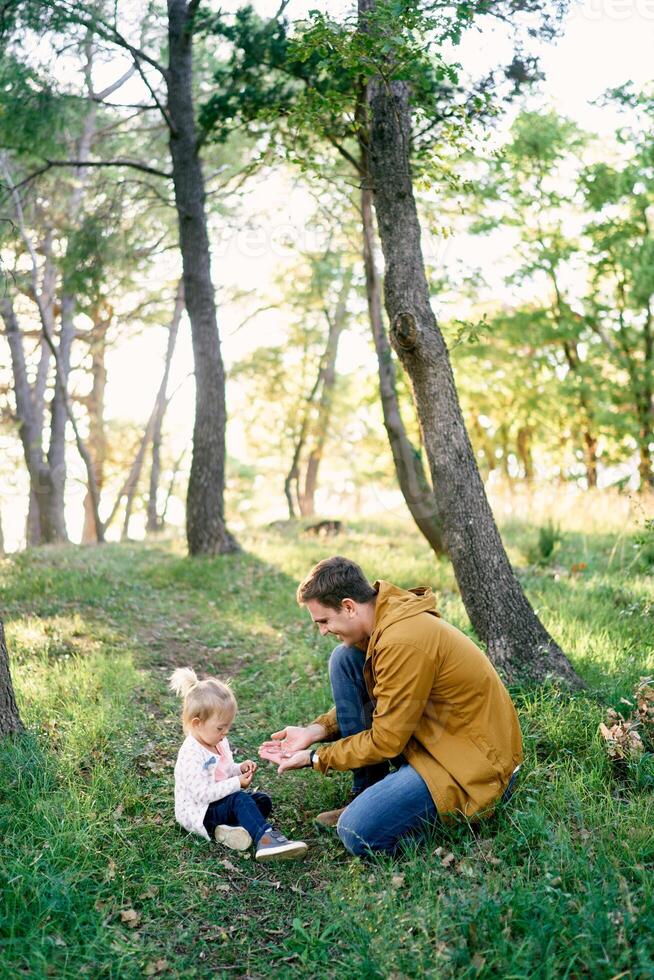 pappa innehar ut svamp till en liten flicka Sammanträde på grön gräs i de skog foto