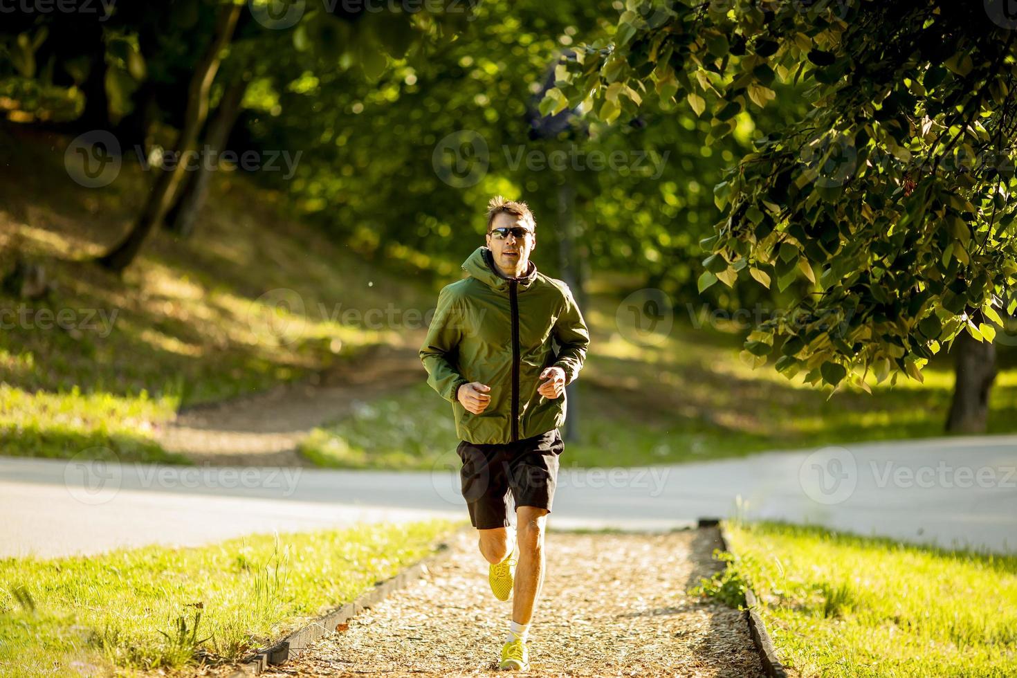 atletisk ung man kör medan du tränar i solig grön park foto