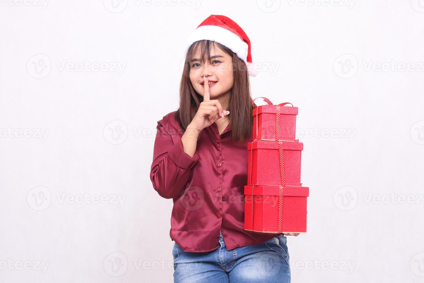 skön ung sydöst asiatisk flicka leende föra 3 lådor av gåvor på jul bär santa claus hatt bär röd skjorta modern tecken be till vara tyst vit bakgrund befordran och reklam foto