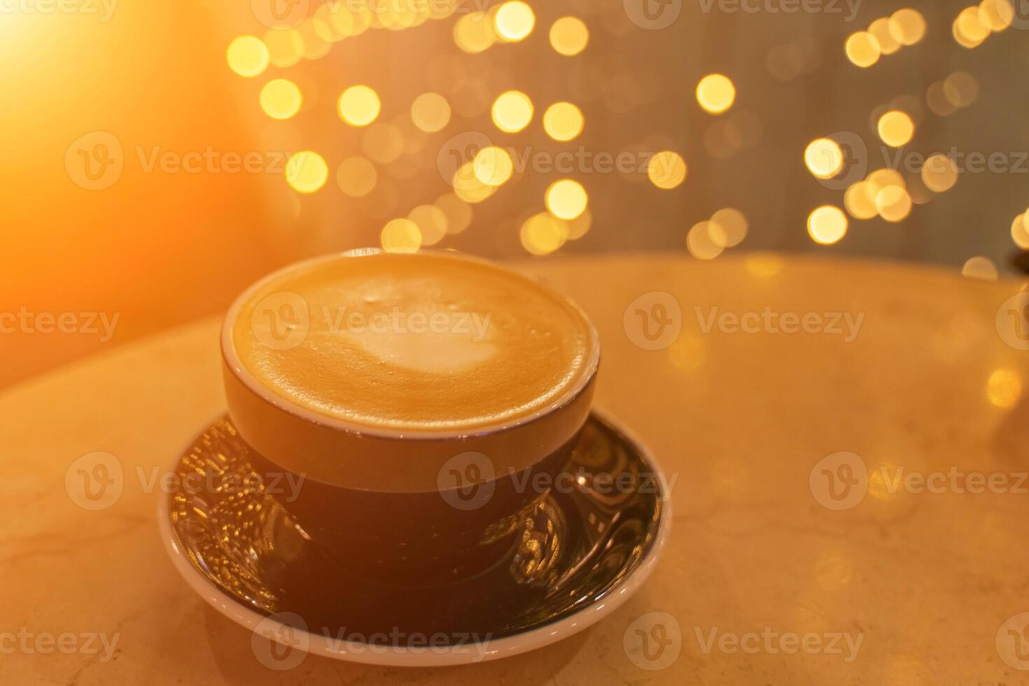 en kopp av latte kaffe med hjärtformade skum på en tabell i en Kafé, i de bakgrund, de lampor i en fläck är reflekterad på de tabell. foto