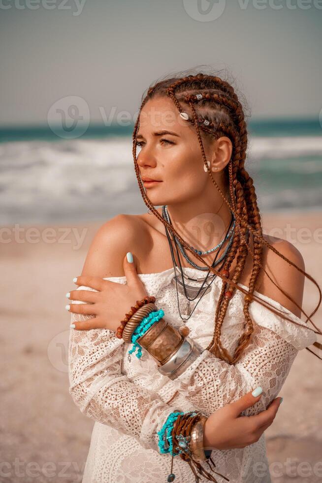 modell i boho stil i en vit lång klänning och silver- Smycken på de strand. henne hår är flätad, och där är många armband på henne vapen. foto