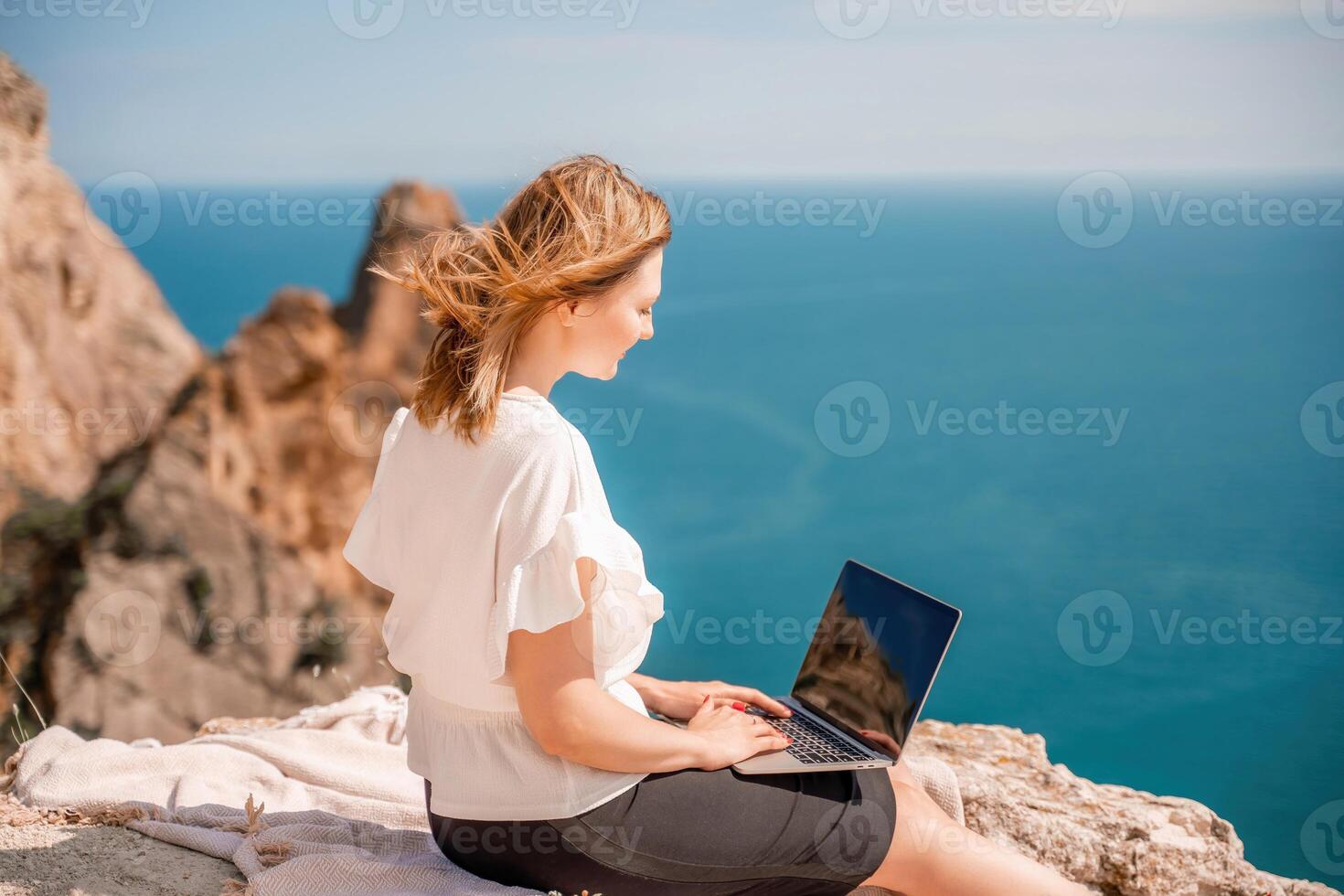frilans kvinnor hav arbetssätt på de dator. Bra ser mitten åldrig kvinna skriver på en bärbar dator tangentbord utomhus med en skön hav se. de begrepp av avlägsen arbete. foto