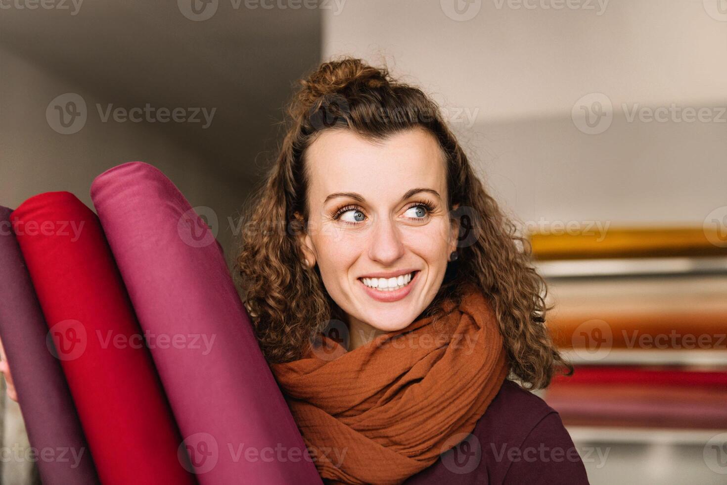 glad uttryck fångad på en kvinna med lockigt hår, bär en värma scarf, med färgrik tyg rullar i de bakgrund foto