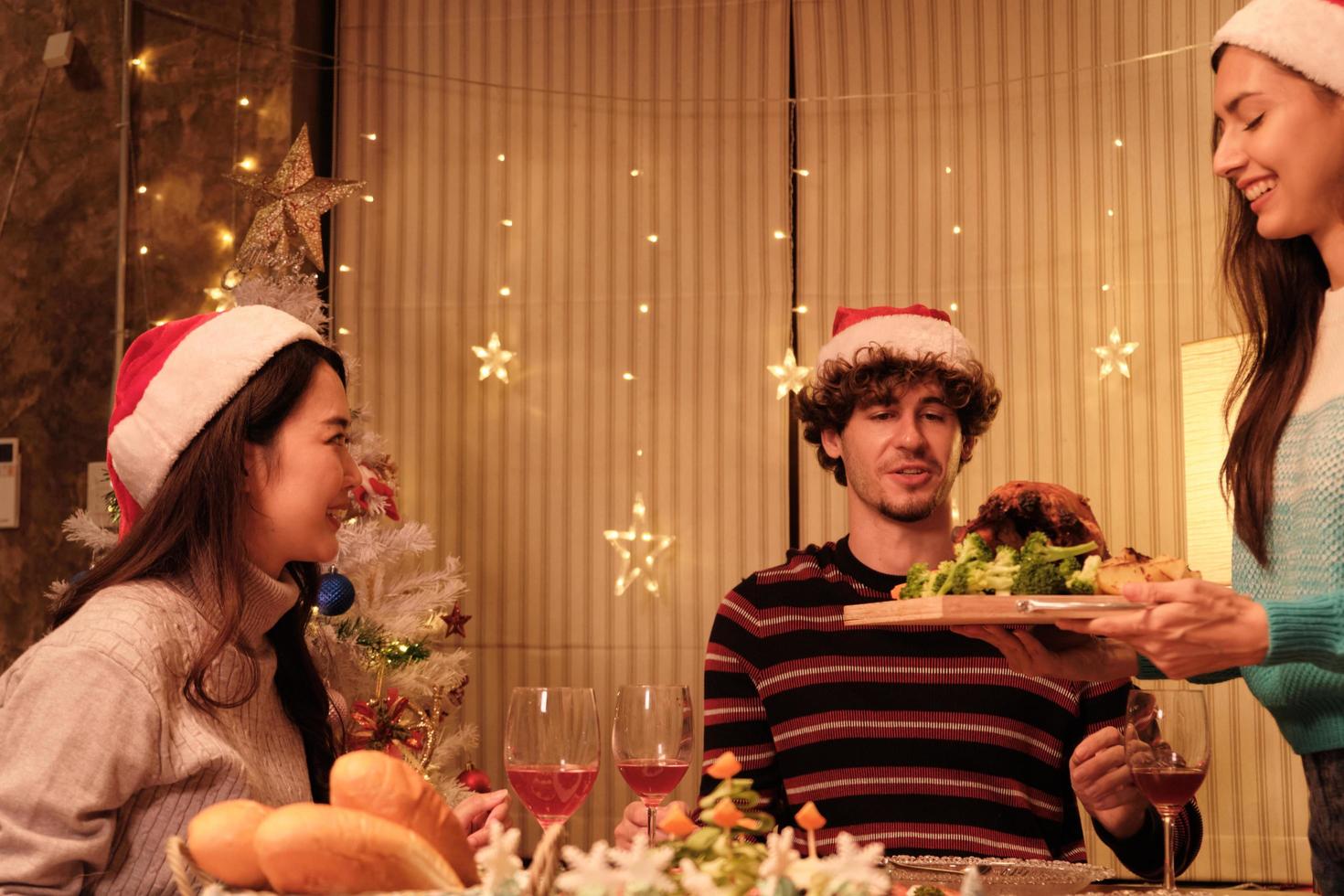 en familjs speciella måltid, ung hona serverar rostad kalkon till vänner och glad med drinkar under en middag hemma i matsalen dekorerad för julfest och nyårsfest. foto