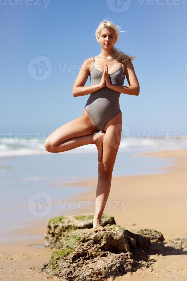 kaukasisk blond kvinna utövar yoga på stranden foto