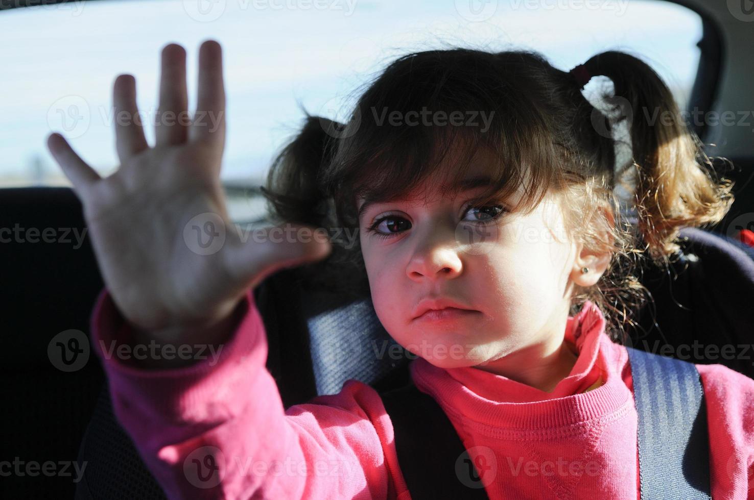 liten flicka som reser med bil sitter i sitt säkerhetssäte foto