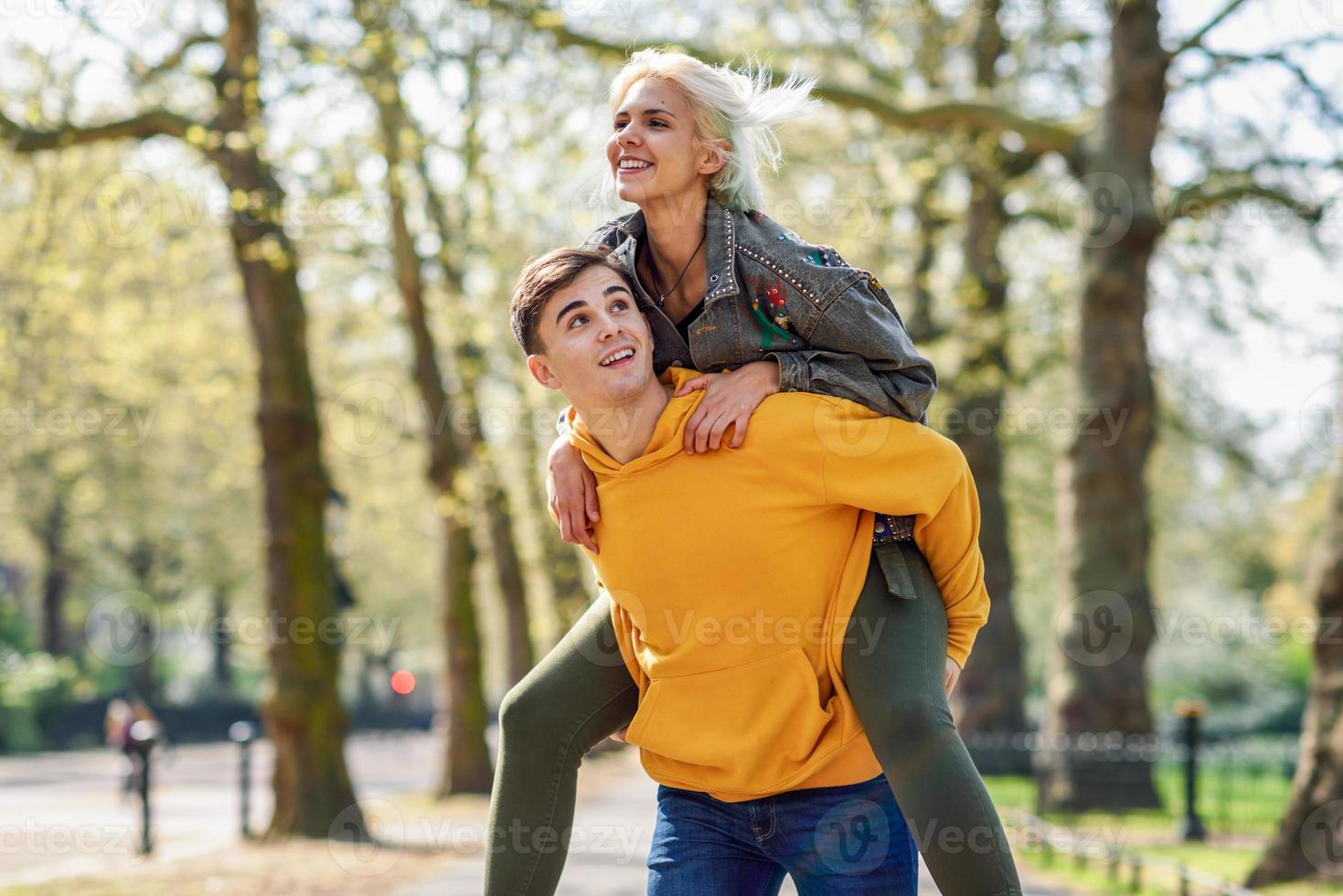 roligt par i en stadspark. pojkvän bär sin flickvän på piggyback. foto