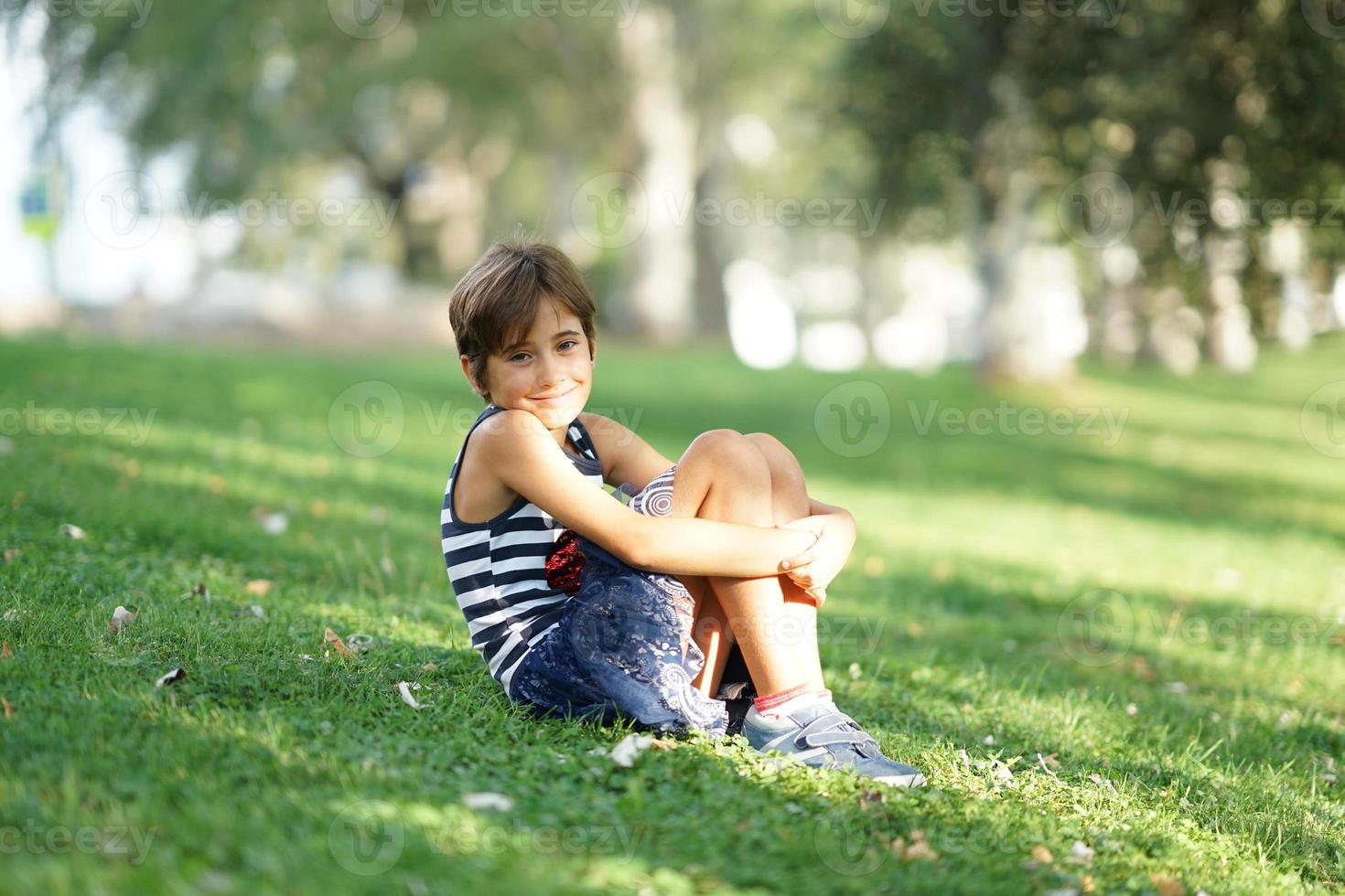 liten flicka, åtta år gammal, sitter på gräset utomhus. foto
