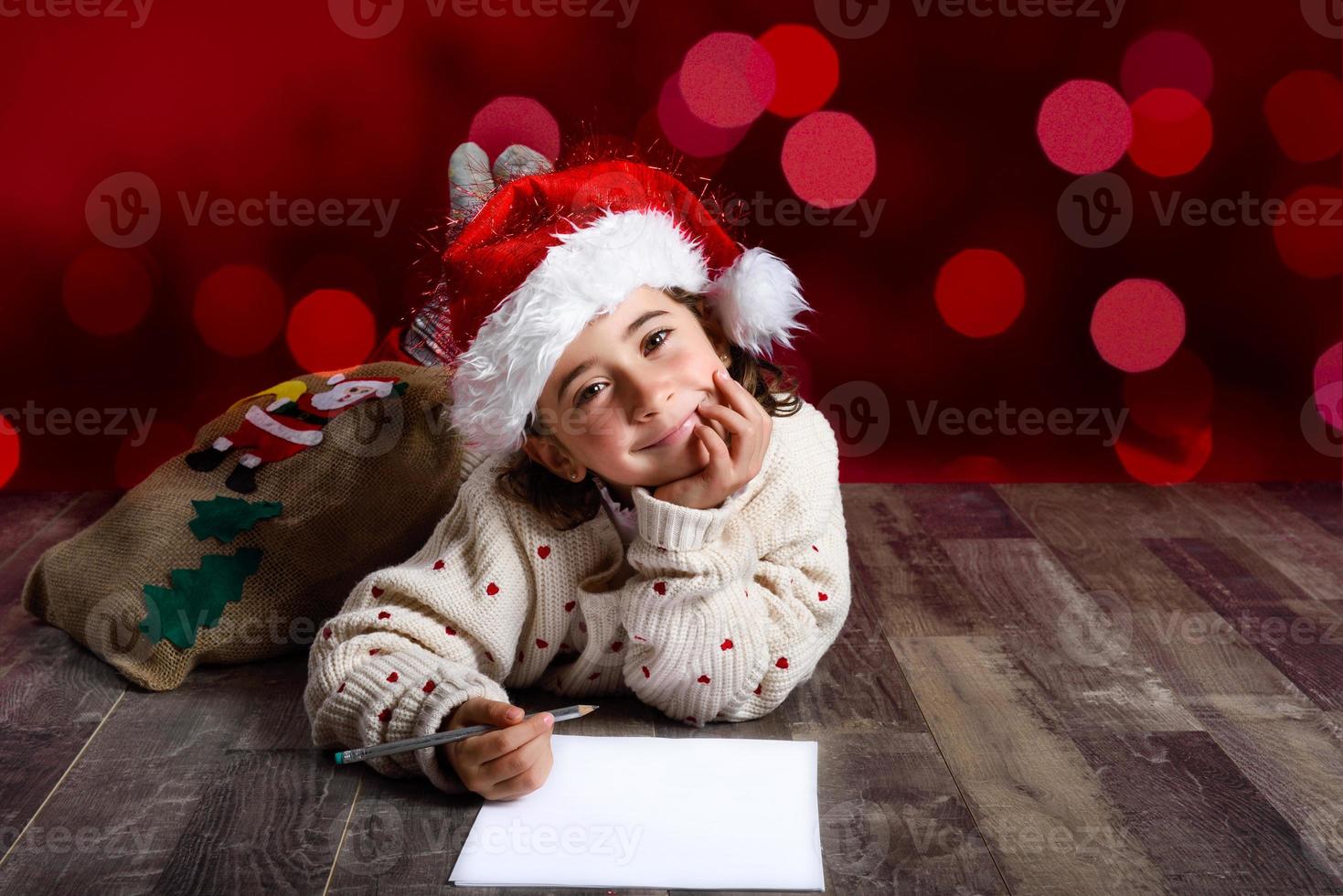bedårande liten flicka bär tomte hatt skriver santa brev foto