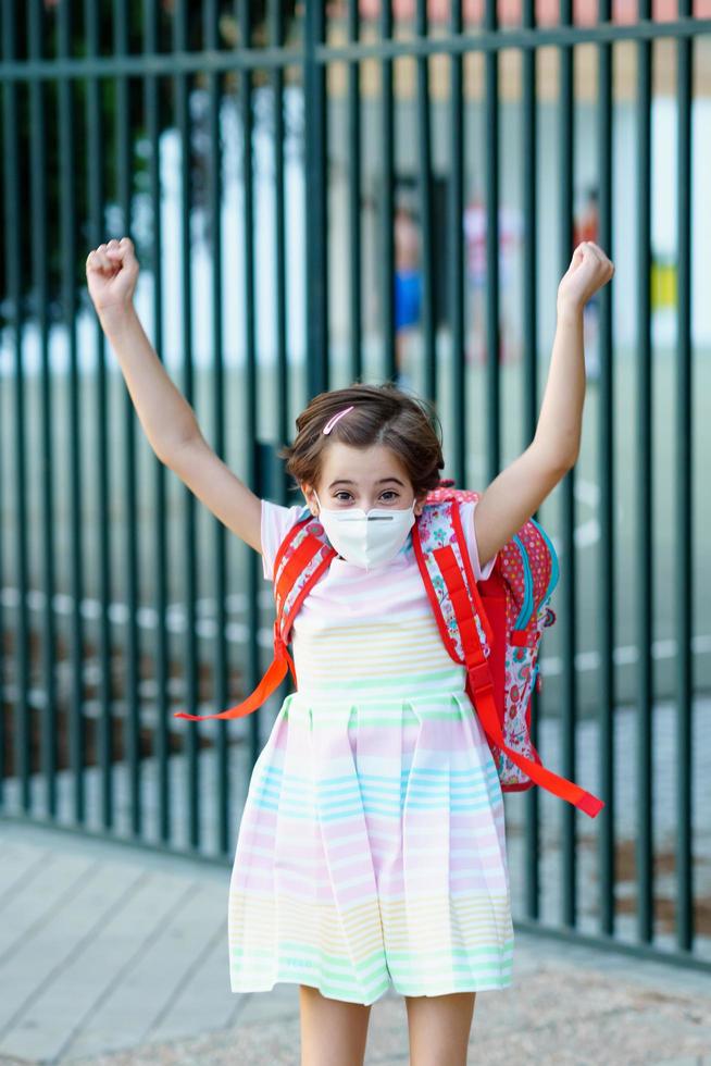 flicka som bär en mask tar ett hopp av glädje över att gå tillbaka till skolan. foto